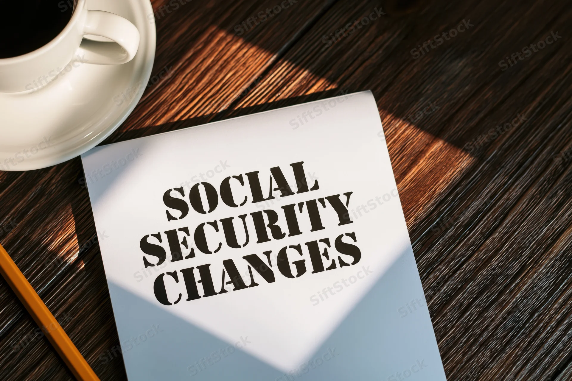 White notepad with bold black text reading social security changes on wooden desk beside coffee cup and pencil