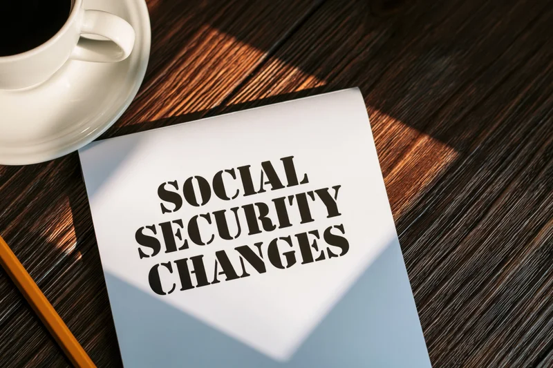 White notepad with bold black text reading social security changes on wooden desk beside coffee cup and pencil