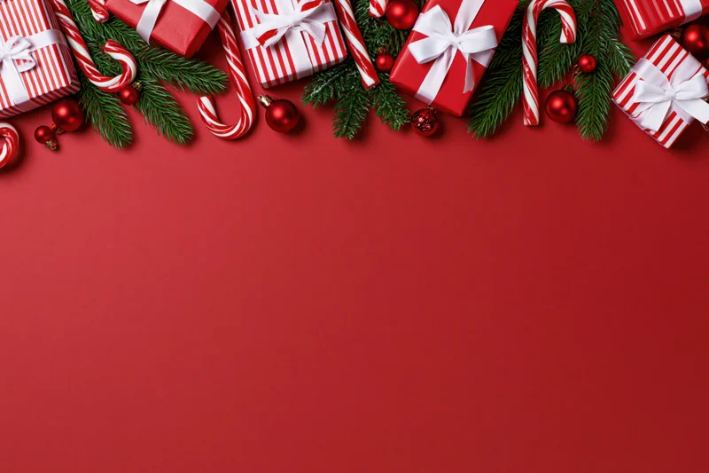Christmas decorations and gift boxes arranged along the top of a red surface with copyspace below
