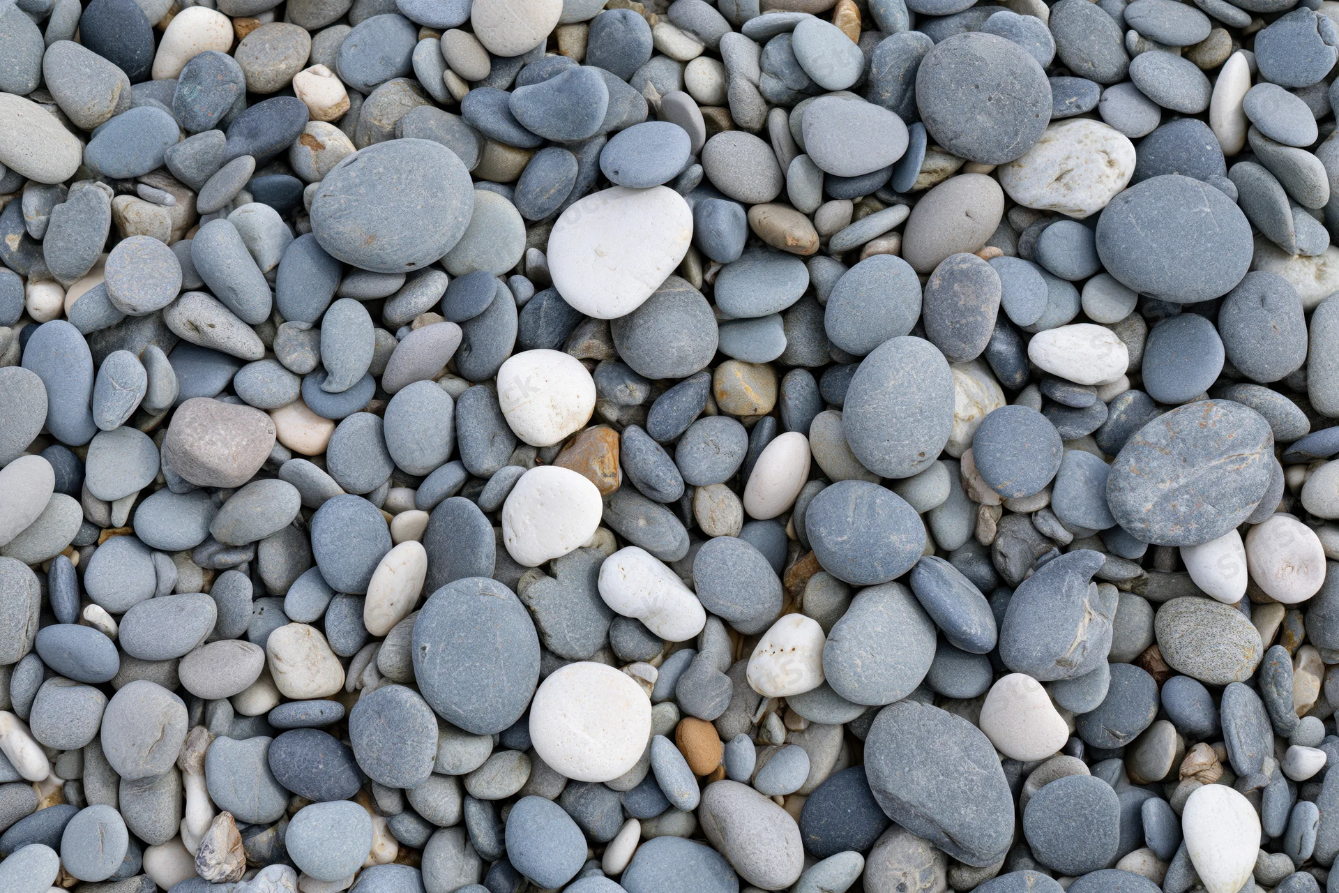 Smooth rounded pebbles scattered across a beach surface in an overhead flat lay view