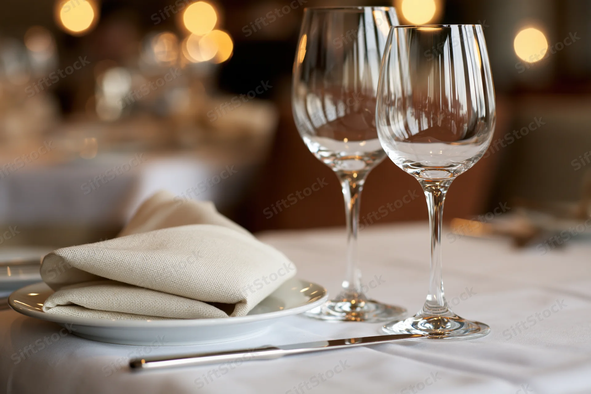 Two empty wine glasses and a folded linen napkin on a white plate at a formally set dining table in a restaurant