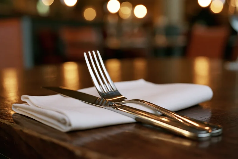 Fork and knife on a folded white napkin on a wooden table in a restaurant