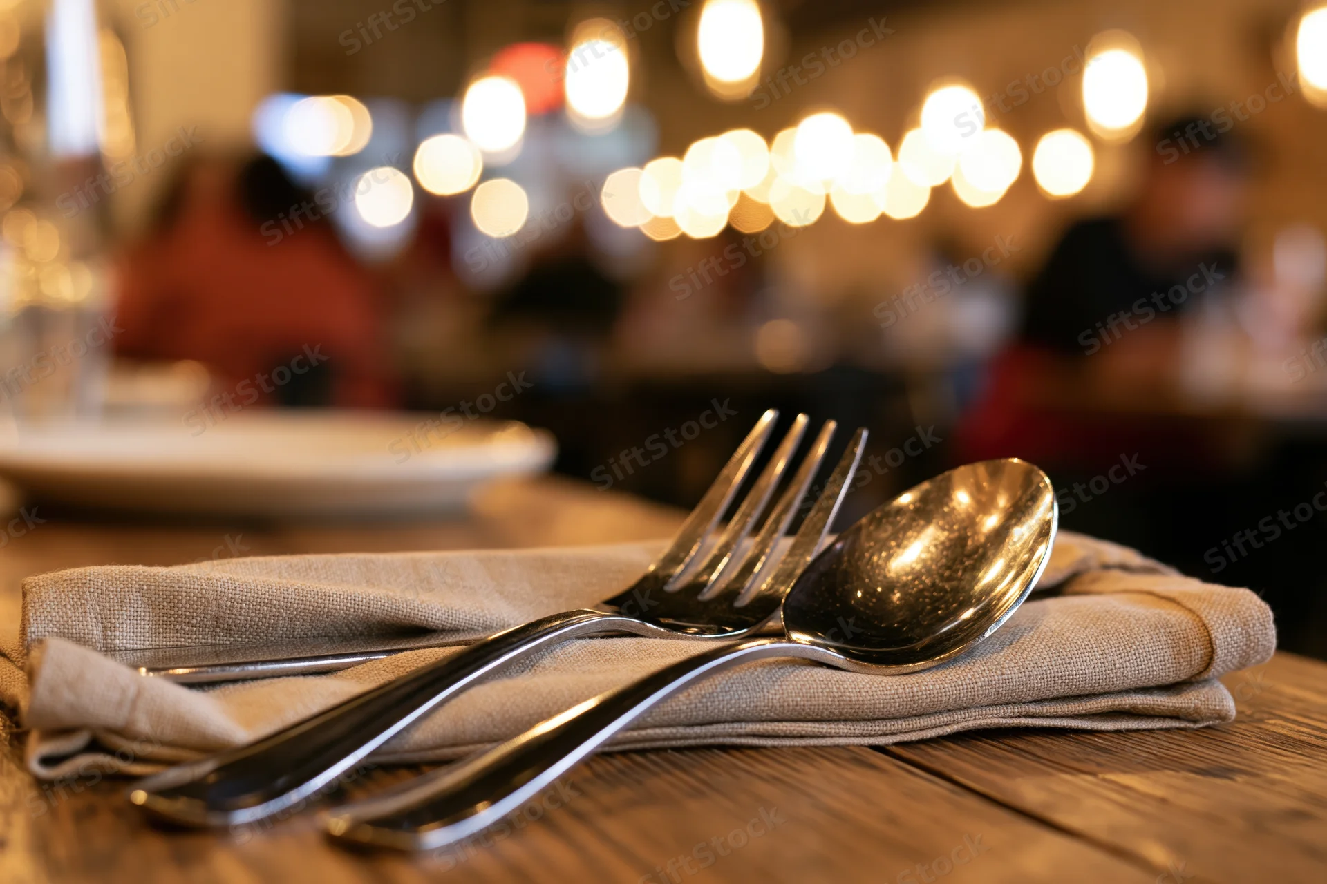 Fork and spoon on a folded linen napkin on a wooden table in a restaurant dining area