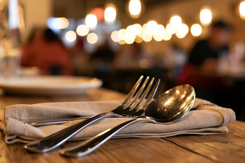 Fork and spoon on a folded linen napkin on a wooden table in a restaurant dining area