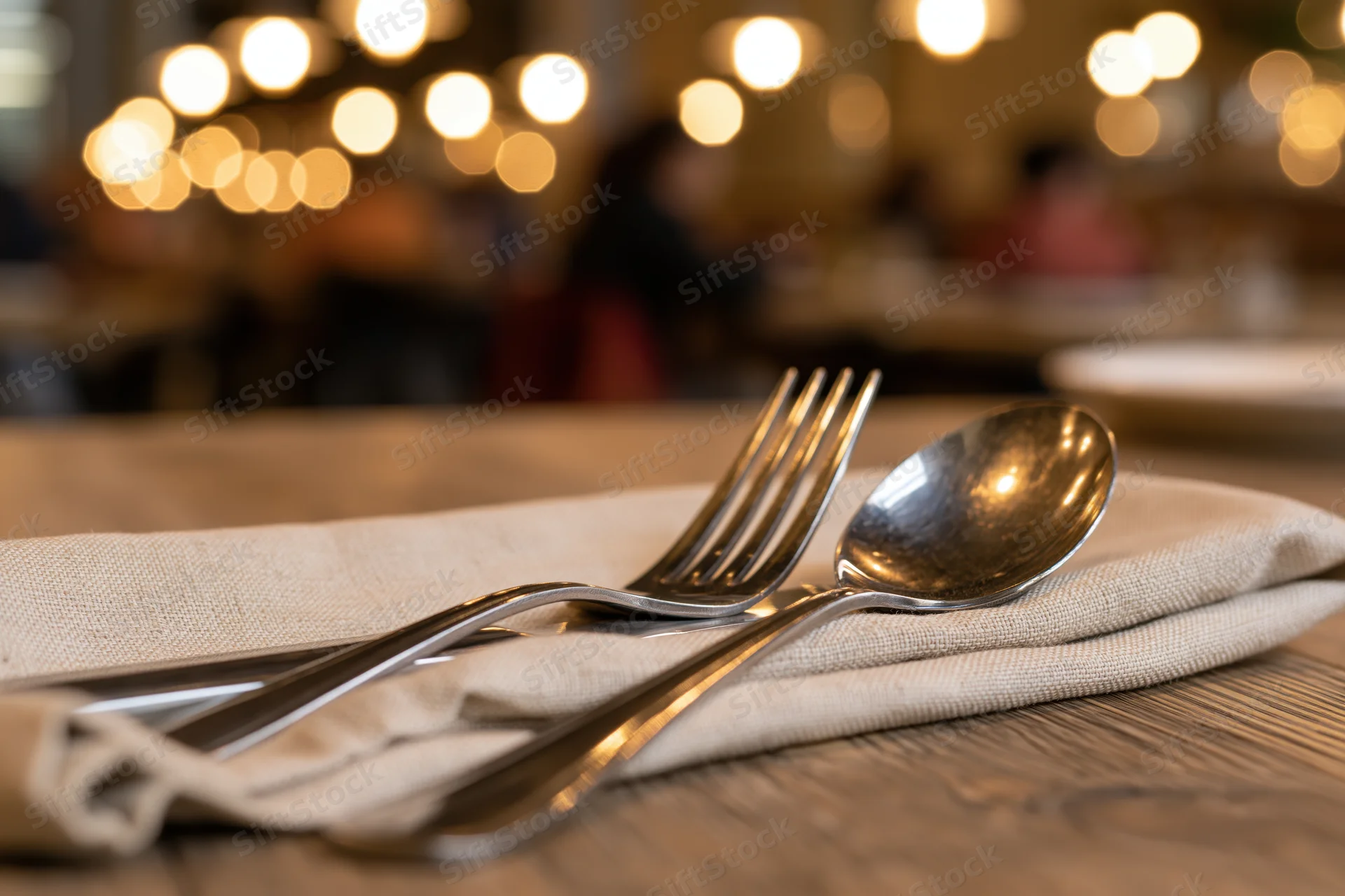 Fork and spoon resting on a folded linen napkin on a wooden table in a restaurant with warm ambient lighting
