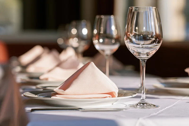 Formal dining table set with white linens, folded peach napkins, wine glasses and silverware in a restaurant