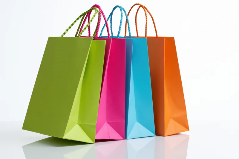 Four colorful paper shopping bags standing and leaning together on a reflective white surface