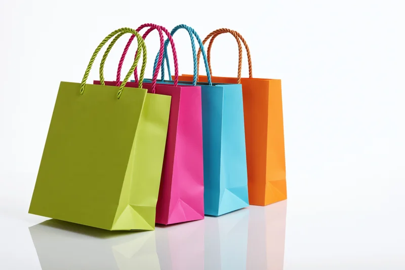 Four colorful paper shopping bags standing and leaning together on a reflective white surface