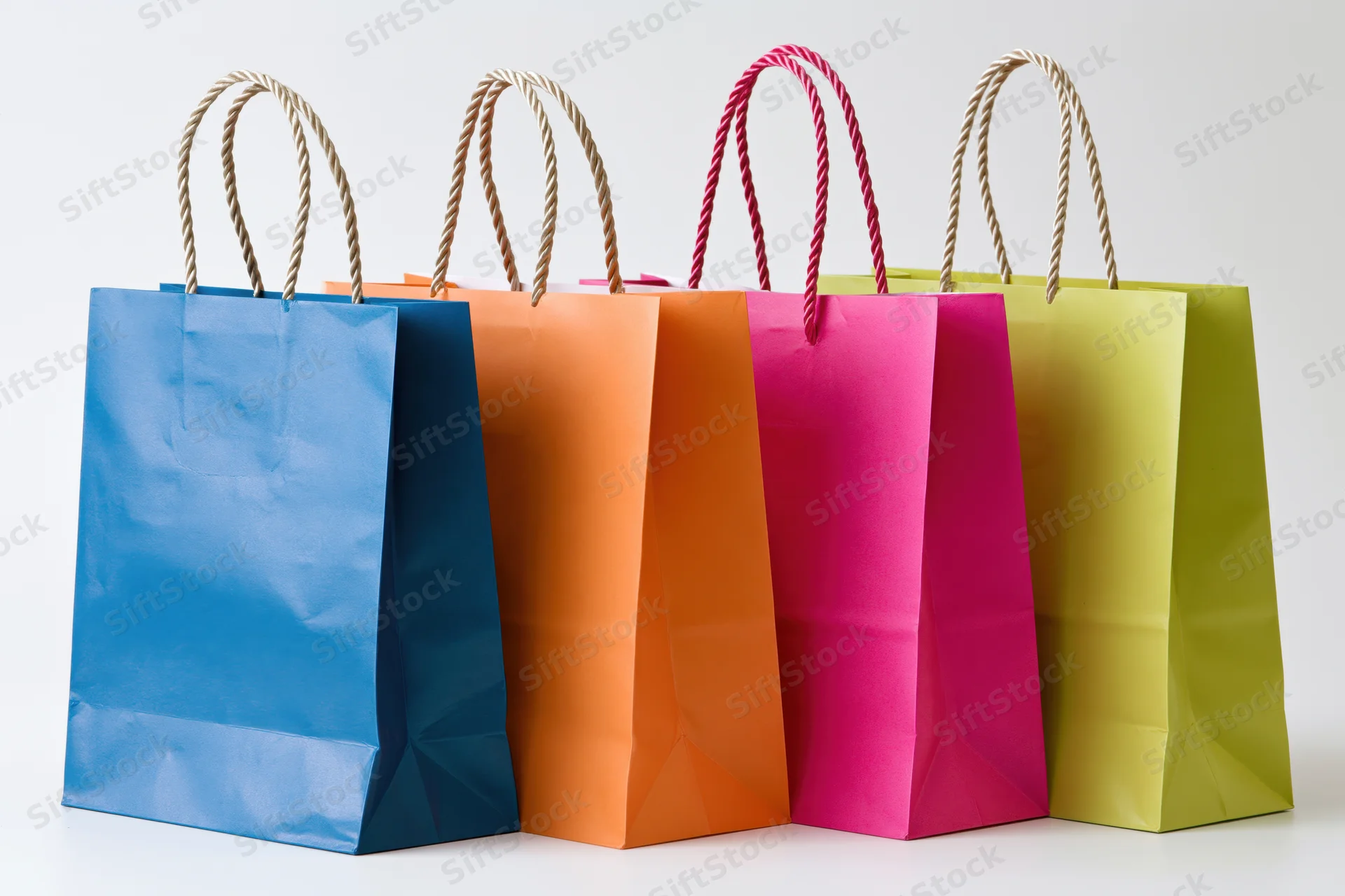 Four colorful paper shopping bags with twisted rope handles arranged in a row on a white background