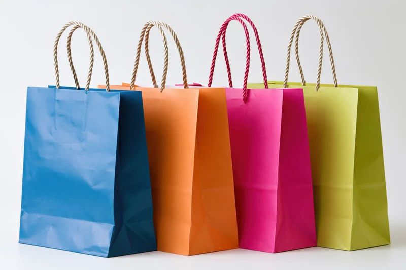 Four colorful paper shopping bags with twisted rope handles arranged in a row on a white background