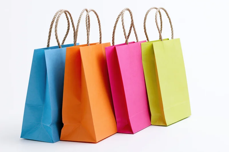 Four colorful paper shopping bags with twisted rope handles standing in a row on white background