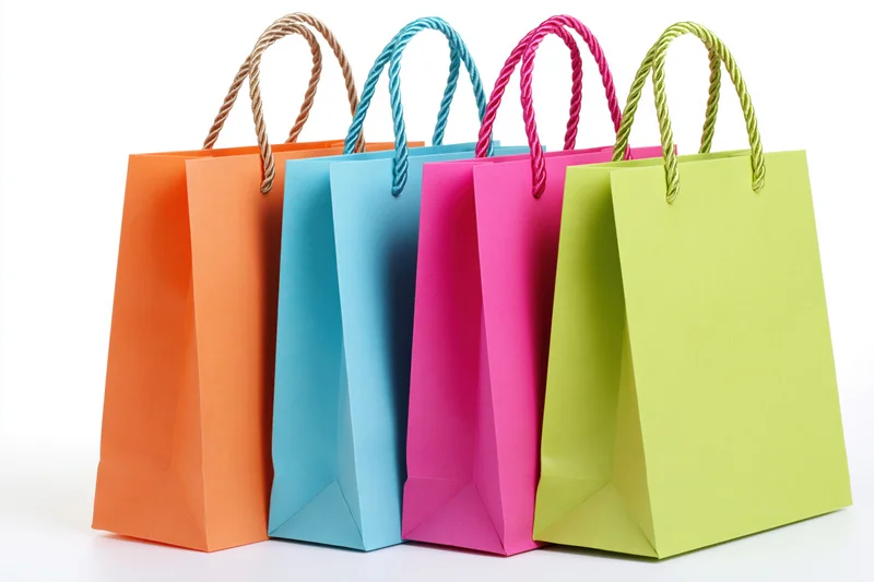 Four colorful paper shopping bags with twisted rope handles arranged in a row on a white background