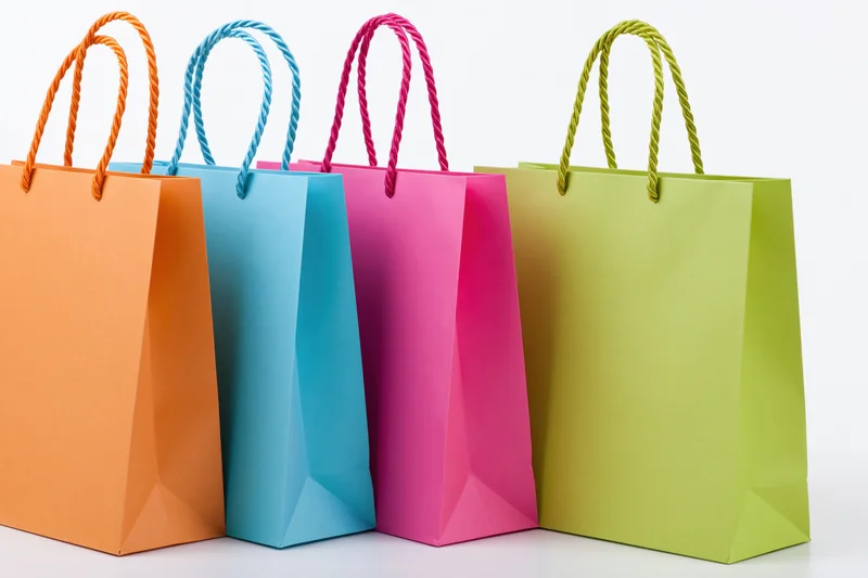 Four colorful paper shopping bags with twisted rope handles arranged in a row on a white background