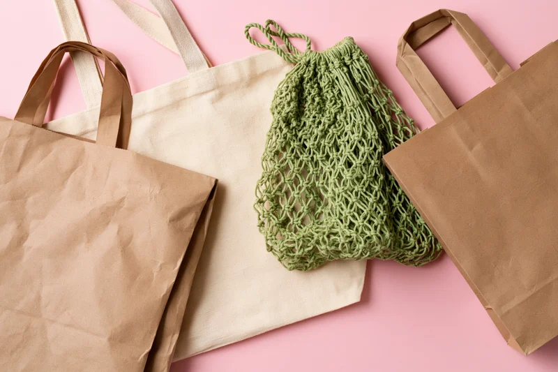 Reusable shopping bags arranged flat on pink surface with copyspace
