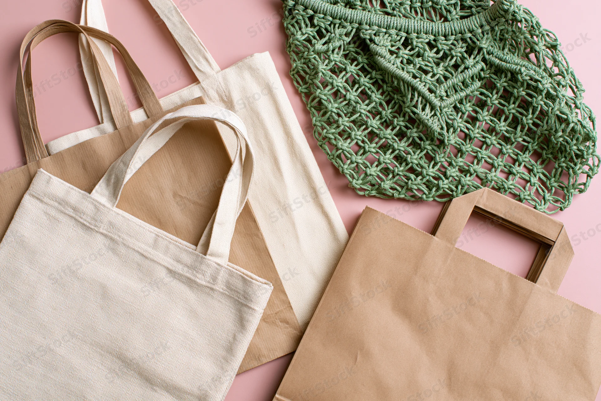 Four reusable shopping bags arranged flat on a pink surface