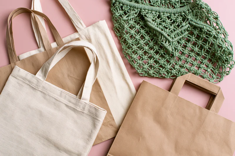 Four reusable shopping bags arranged flat on a pink surface