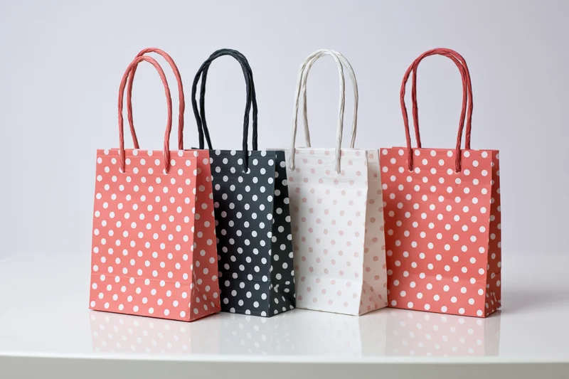 Four small paper gift bags with white polka dots arranged in a row on a white surface