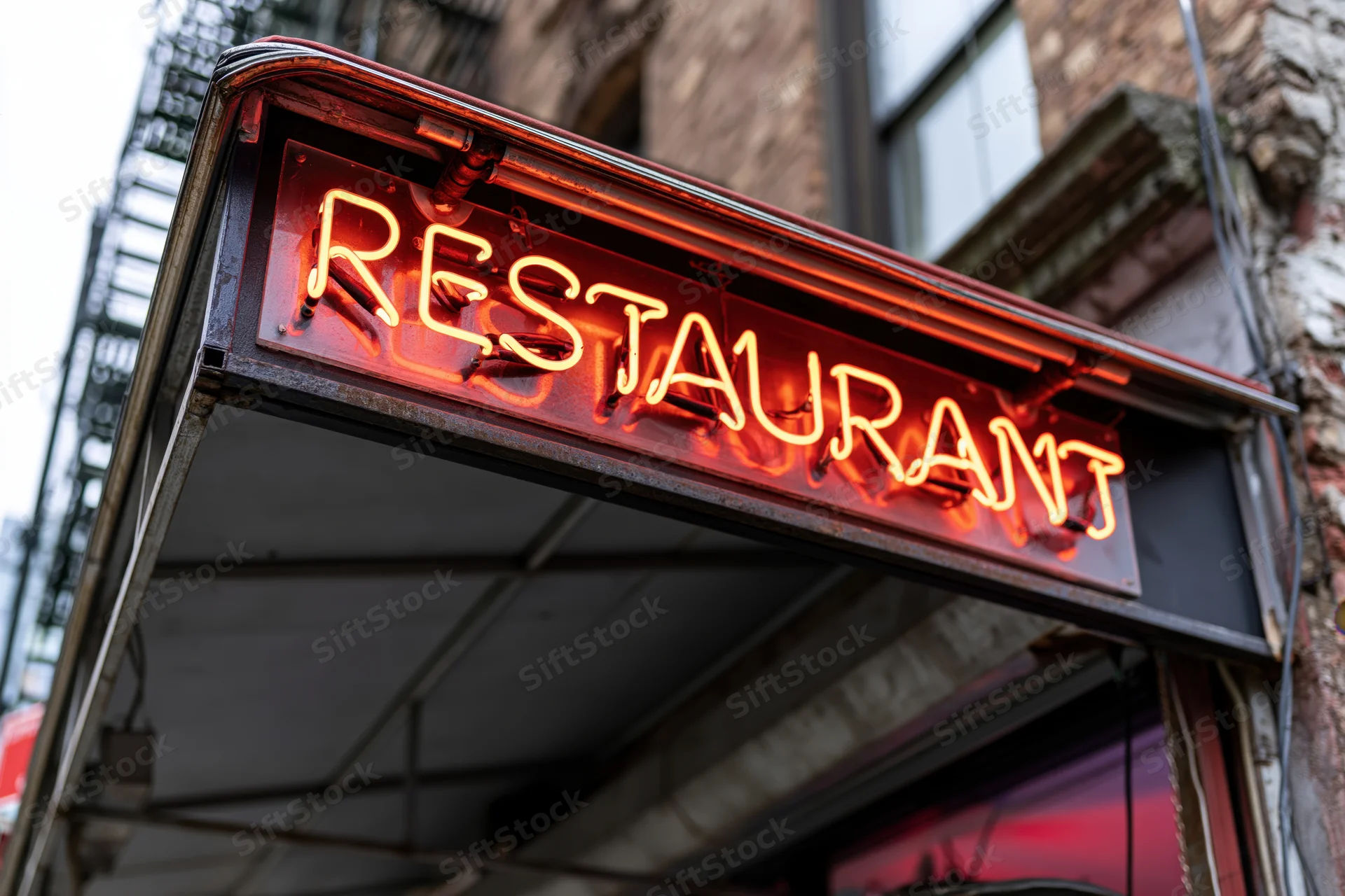 Glowing red-orange neon restaurant sign mounted on a dark metal frame above a brick building entrance
