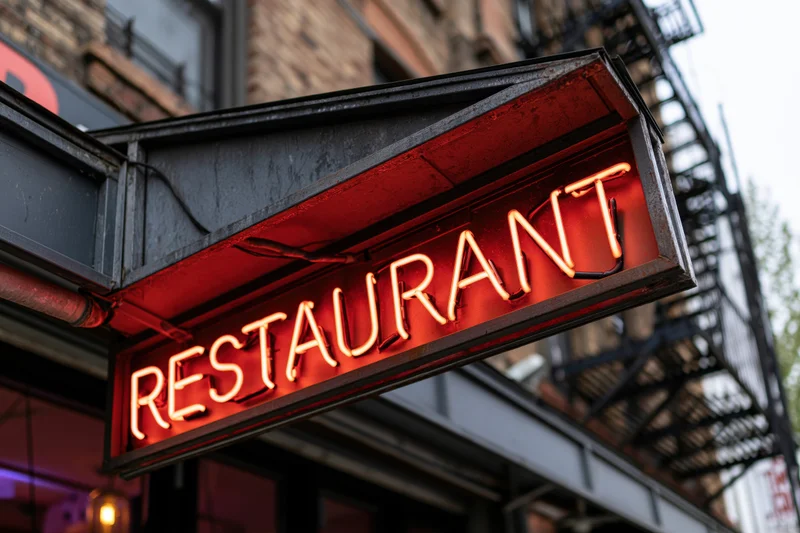 Glowing red-orange neon restaurant sign mounted on a dark metal frame outside a brick building