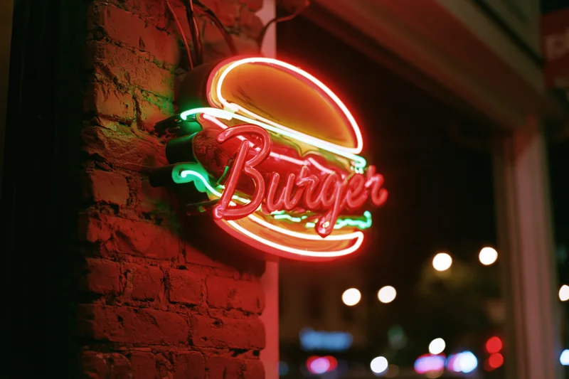 Glowing red neon burger sign mounted on a brick wall at night