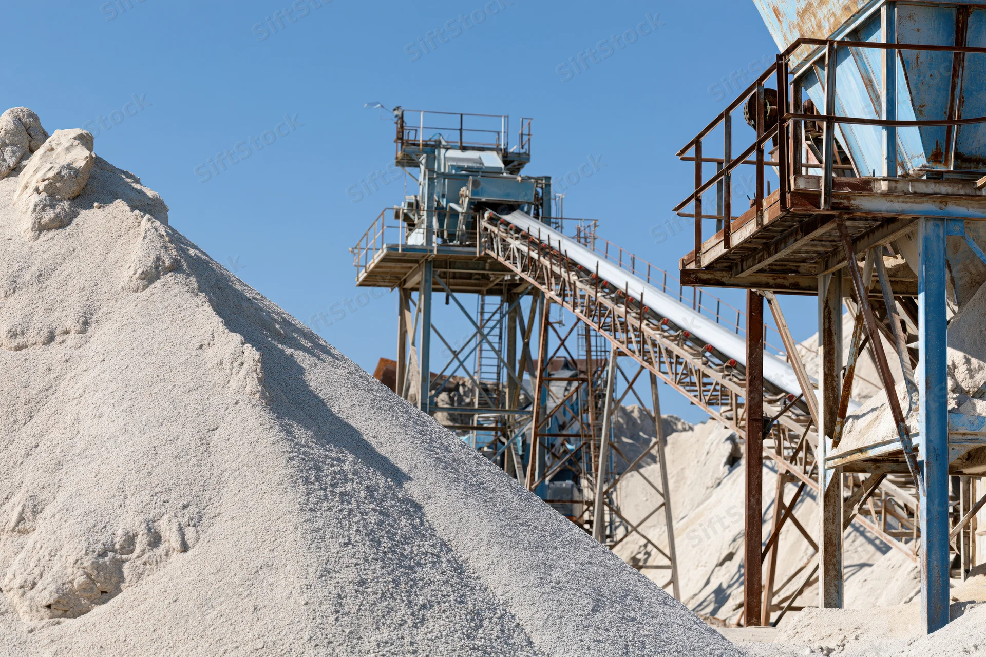 Gravel pile in foreground with conveyor belt machinery rising above in quarry setting