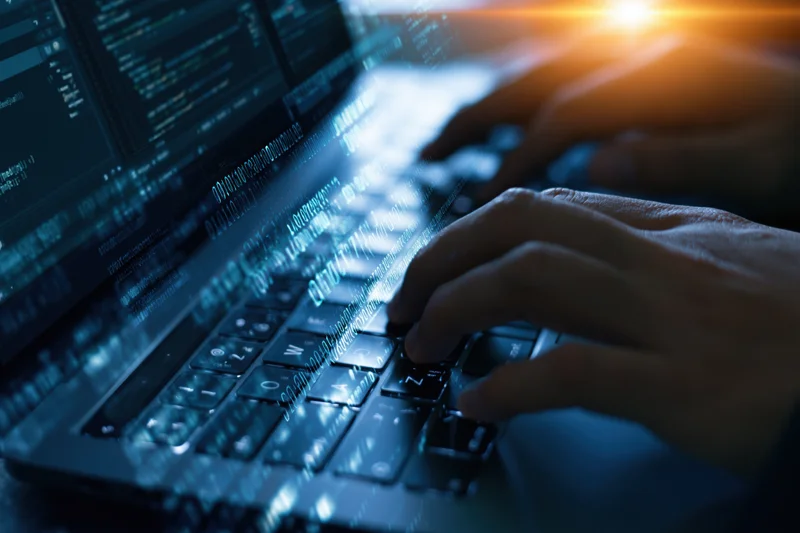 Hands typing on a laptop keyboard with digital code overlay in a dark setting