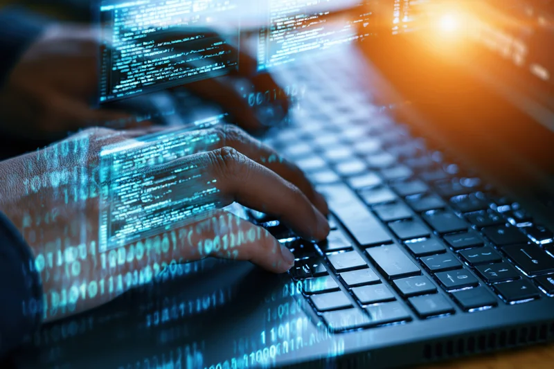 Hands typing on a dark laptop keyboard with digital code overlay