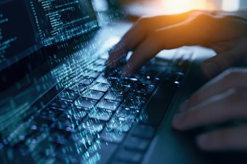 Hands typing on a laptop keyboard with digital code overlay in a dark setting