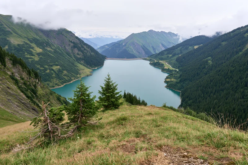 Alpine reservoir nestled between steep green mountains viewed from grassy hilltop