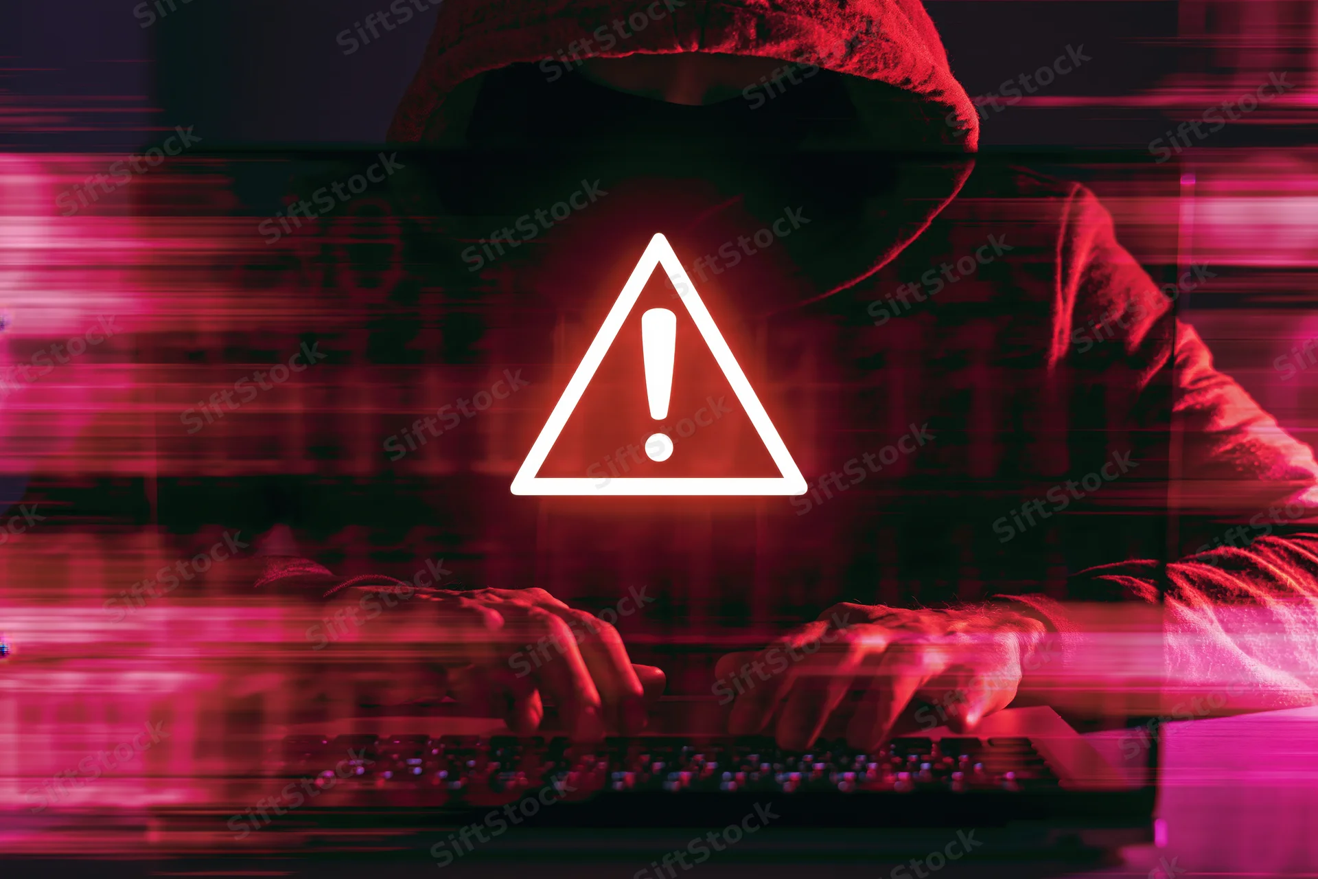 Hooded figure typing on laptop keyboard with warning symbol in dark red digital environment