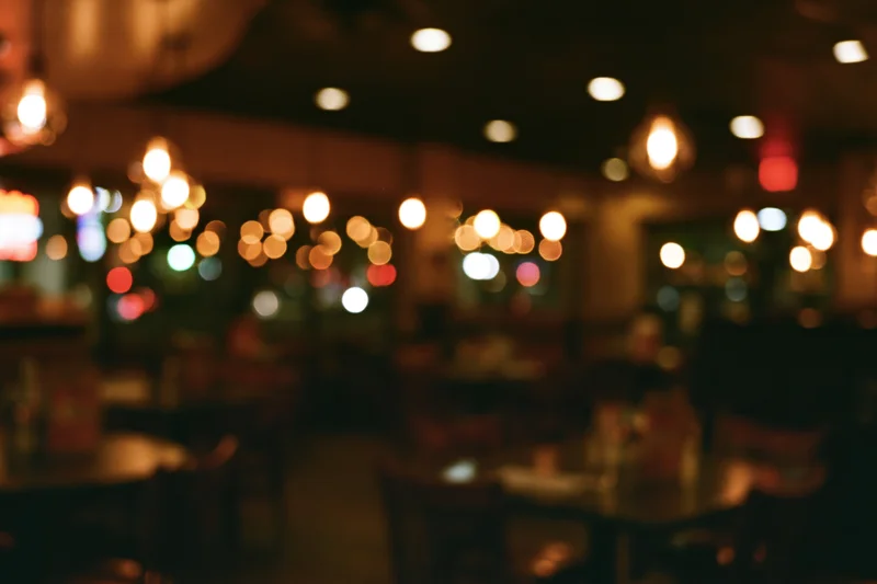Blurred interior of empty restaurant at night with warm bokeh lights and wooden tables