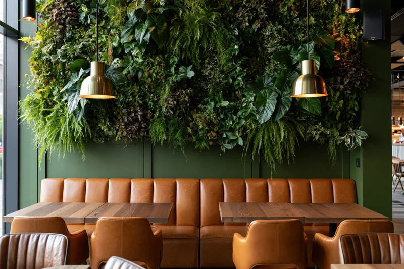 Modern cafe dining area with leather booths and wooden tables beneath a lush green living wall and brass pendant lights