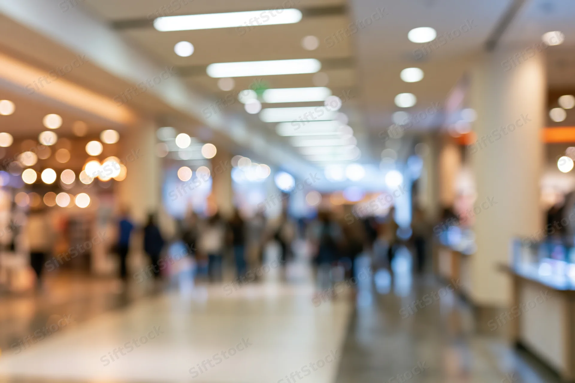Blurred view of a modern retail mall corridor with people walking and storefronts along the sides