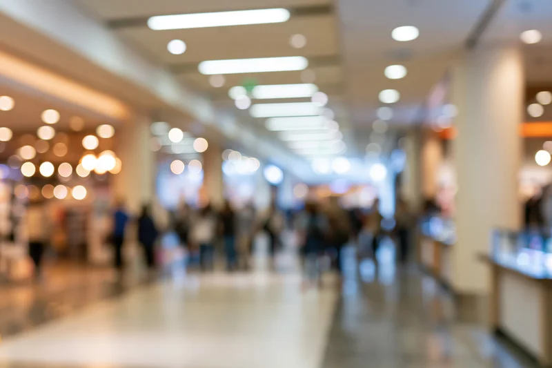 Blurred view of a modern retail mall corridor with people walking and storefronts along the sides