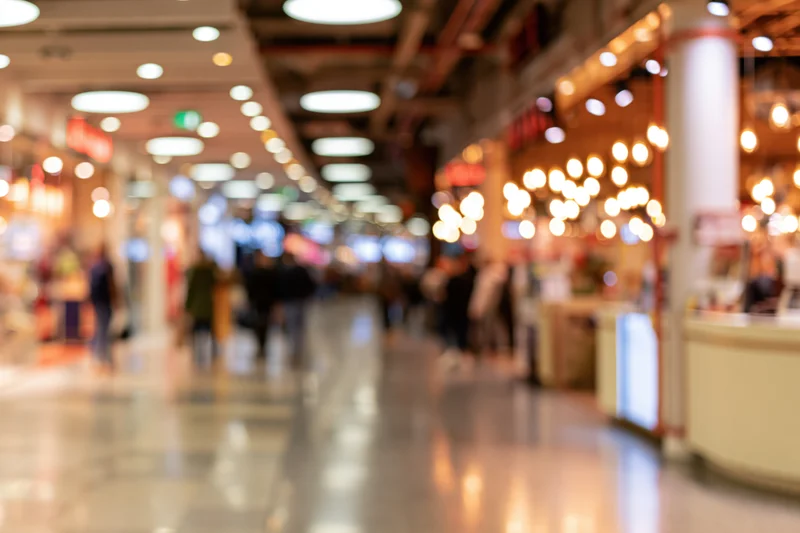 Blurred interior of a modern retail mall corridor with people walking and illuminated storefronts