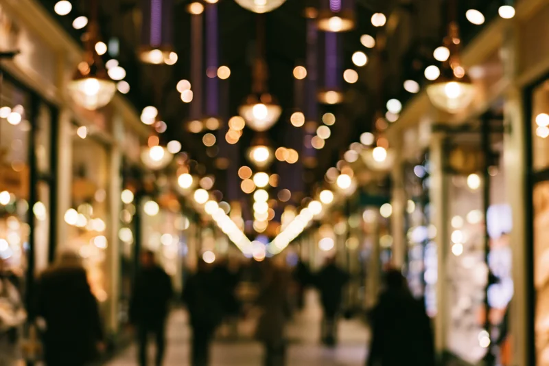 Blurred view of people walking through a shopping mall corridor at night with glowing lights and storefronts