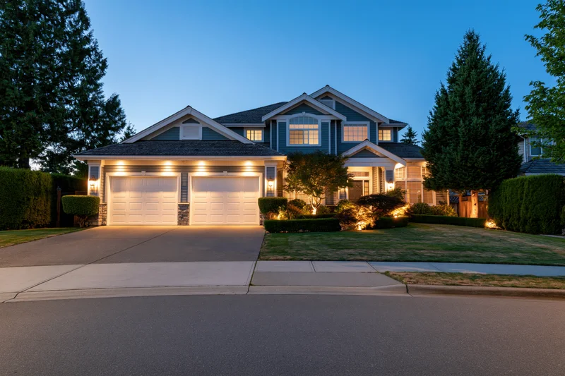 Two-story suburban house facade at dusk with illuminated garage and landscaping