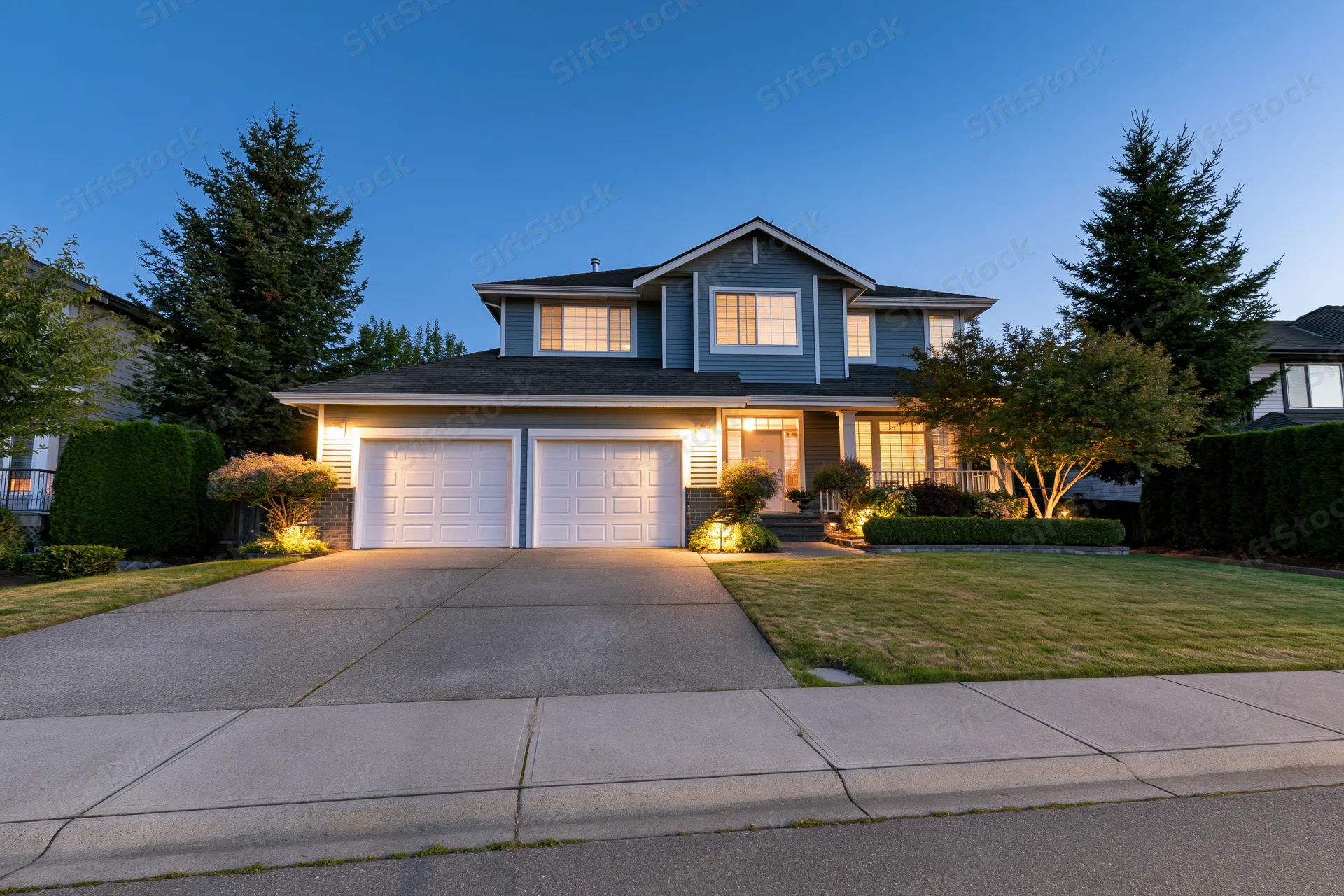 Two-story suburban house facade at dusk with illuminated windows and driveway