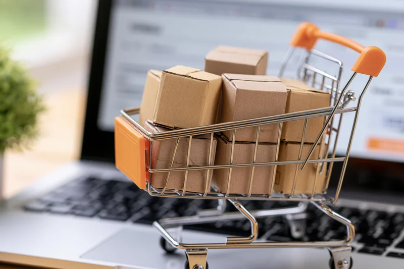 Miniature metal shopping cart filled with small cardboard boxes on laptop keyboard