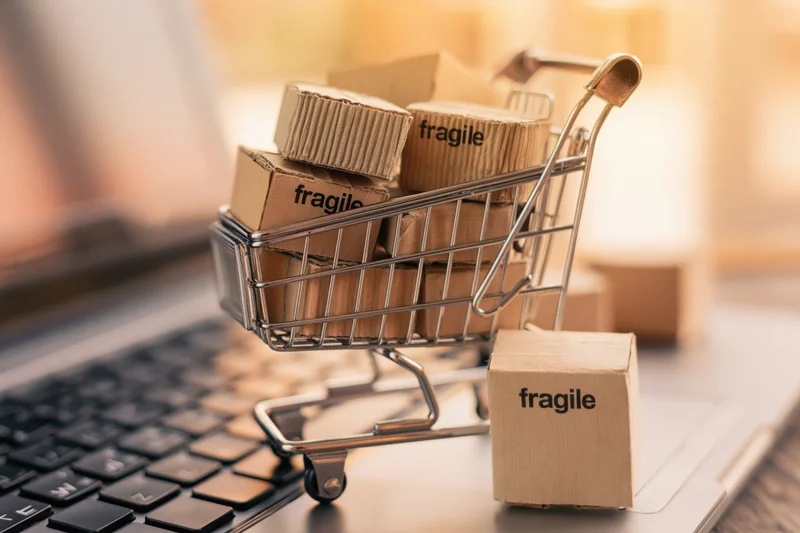 Miniature shopping cart filled with fragile cardboard boxes on a laptop keyboard