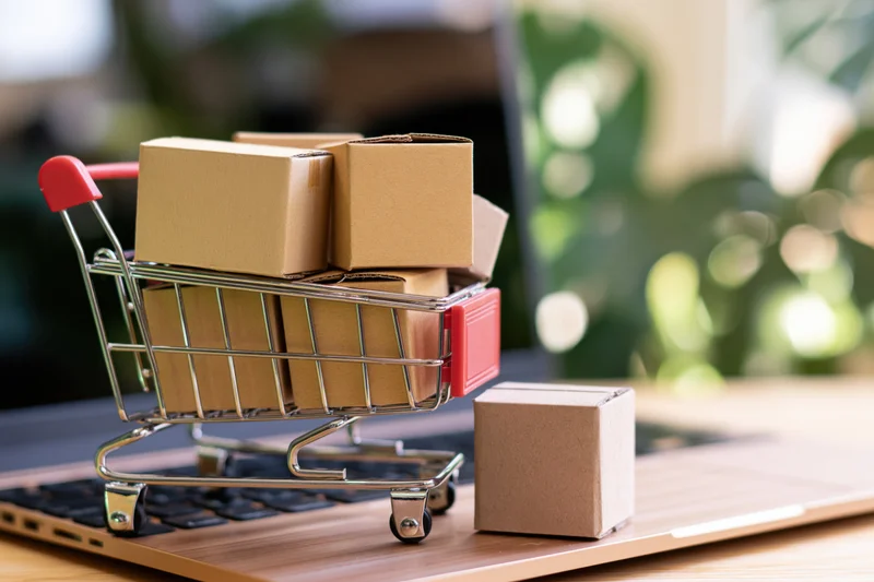 Miniature shopping cart filled with cardboard boxes on a laptop keyboard