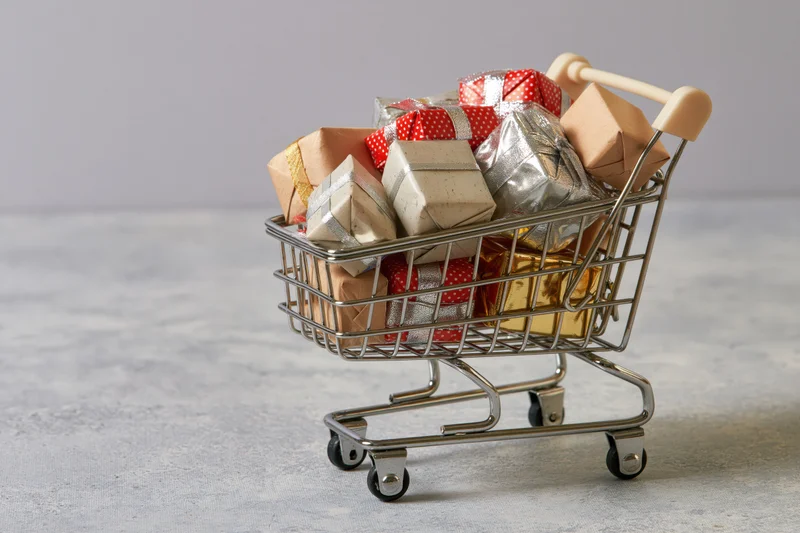 Miniature metal shopping cart filled with wrapped gifts on a textured surface