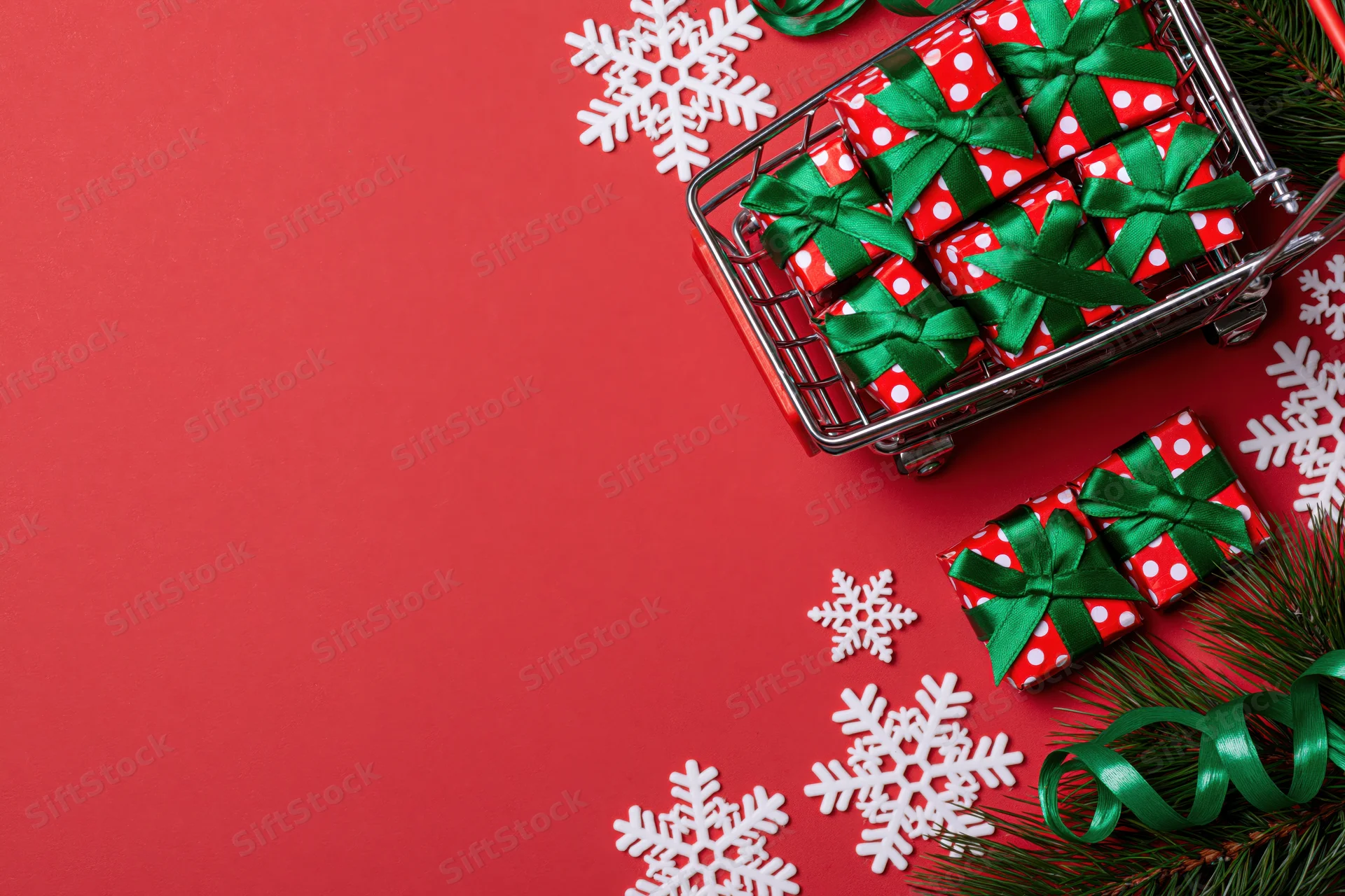Miniature shopping cart filled with wrapped gifts and holiday decor on red background