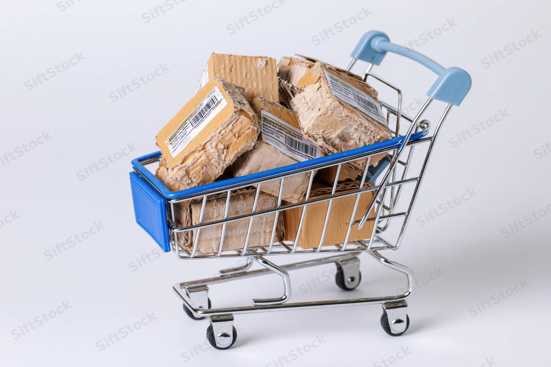 Miniature metal shopping cart filled with cardboard boxes on white background