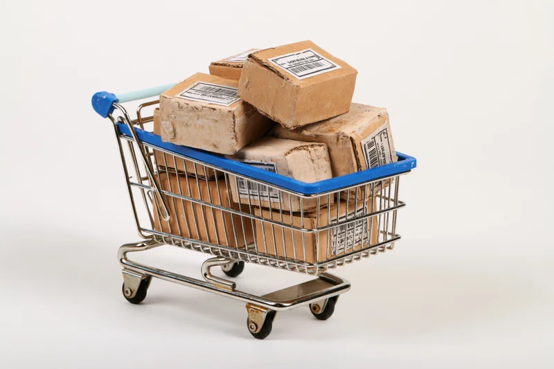 Miniature metal shopping cart filled with cardboard boxes on white background