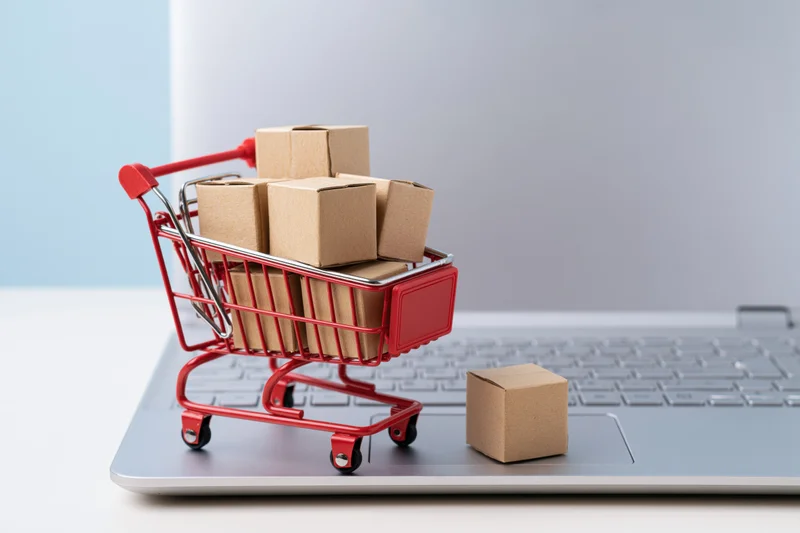 Miniature red shopping cart filled with kraft boxes on a laptop keyboard