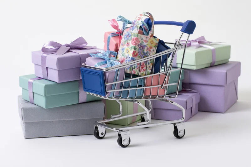Miniature shopping cart filled with colorful wrapped gift boxes on white background