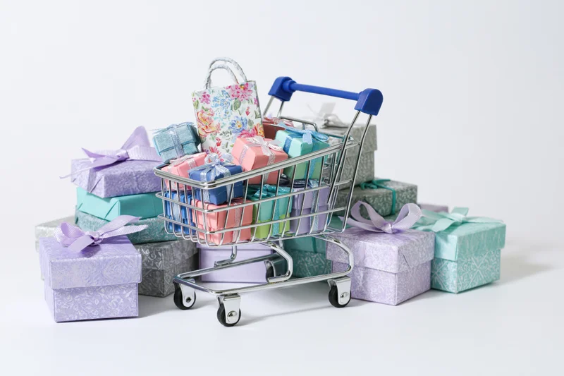 Miniature silver shopping cart filled with colorful gift boxes on white background
