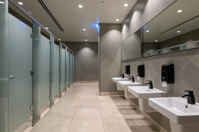 Modern public restroom interior with row of white wall-mounted sinks and frosted glass partitions