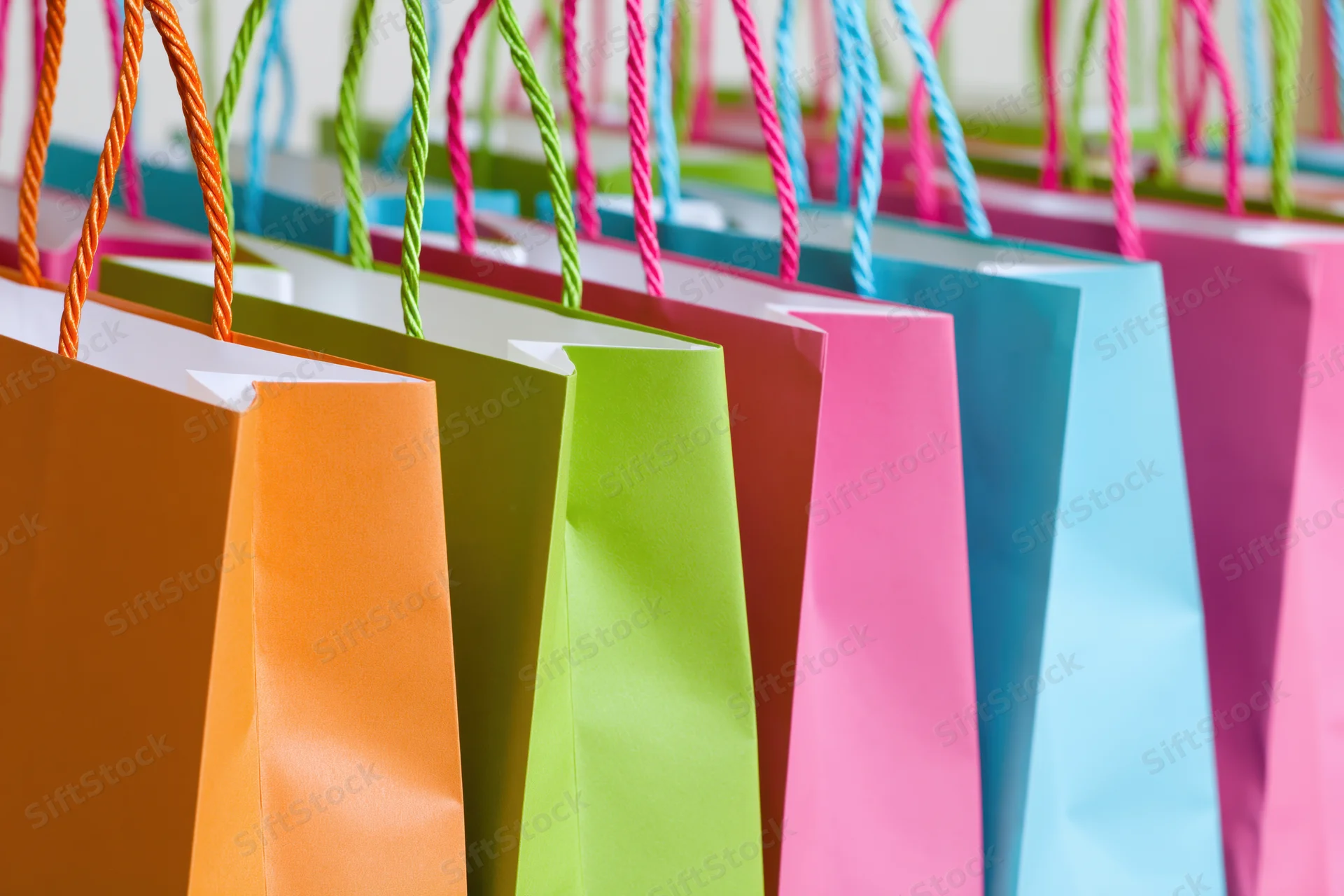 Colorful paper shopping bags standing upright in a row, arranged side by side, showcasing vibrant hues and twisted handles